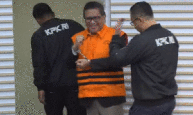 
					Di depan kamera wartawan Sekjen PDI-P, Hasto Kristiyanto mengangkt kedua tangannya yang diborgor sambil tersenyum, saat konferensi pers di gedung Merah-Putih KPK, Kamis 20 Februari 2025. Tangkap Layar Video Youtube@VivaNews