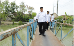 Bupati Jombang, H Warsubi menyeberangi jembatan kecil sepanjang 27 me di dusun Dusun Banjarejo, Desa Kudubanjar, Kecamatan Kudu, Kabupaten Jombang, Rabu 31 Desember 2025. Ia berencana membangun jembatan tersebut pada anggaran 2026. Foto: swrawajombang.com/ elok apriyanto